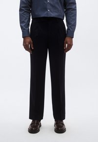 Tamsiai mėlyni laisvo silueto kelnės su klostėmis priekyje, derinamos su džinsiniu marškinių tipo palaidine ir tamsiai rudos spalvos loaferiais. Lygus audinio tekstūra.