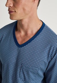 Blauwe V-hals tshirt met een geometrisch patroon van kleine diamanten. Zachte stof en contrasterende blauwe halslijn. Korte mouwen.