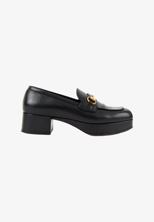 Mocassin à plateforme en cuir noir avec un petit talon bloc et un détail en métal doré en forme de mors de cheval à l'avant.