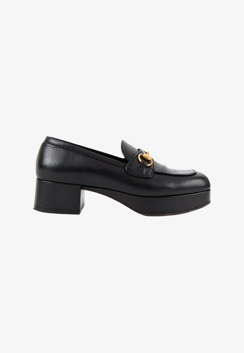 Mocassin à plateforme en cuir noir avec un petit talon bloc et un détail en métal doré en forme de mors de cheval à l'avant.