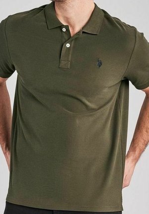 Polo vert olive en coton. Il présente une patte de boutonnage à trois boutons, des manches courtes et un petit logo sombre sur la poitrine.