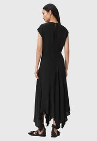 Černé splývavé šaty s krátkými rukávy, asymetrickým lemem a detaily v oblasti klíčové díry na zádech. V kombinaci s černými plochými sandály. Hladká textura.