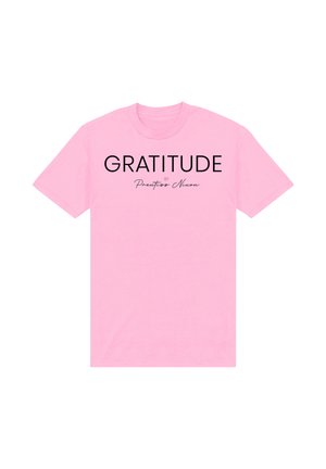 T-shirt rosa a maniche corte con testo nero "GRATITUDE" e la scritta più piccola "by Prentiss Nixon" in corsivo, centrata sul davanti.