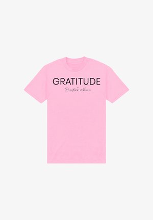 T-shirt rosa a maniche corte con testo nero "GRATITUDE" e la scritta più piccola "by Prentiss Nixon" in corsivo, centrata sul davanti.