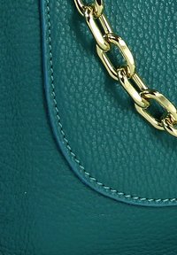 Turkooise leren handtas met een getextureerd oppervlak, een gouden kettingband en contrasterende blauwe stiknaden langs de randen.