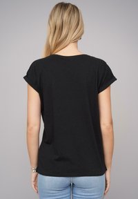 Svart kortermet t-skjorte med rullekrager, laget av myk bomull. Har en ledig passform og en buet kant. Brukt sammen med lyseblå jeans.