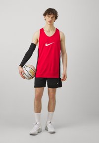 Punane Nike korvpalli tank tops mustade külgtaskutega, mustad lühikesed püksid, must käevars ja korvpall. Seljas on valged spordijalatsid ja sokid.