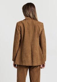 Blazer in ciniglia marrone con vestibilità su misura, caratterizzato da un colletto a revers e spalle strutturate, con trama visibile e costine verticali.