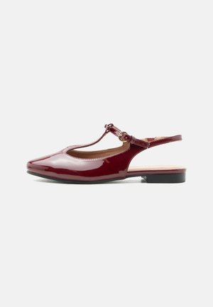 Glanzende bordeauxrode lage hak T-band slingback schoen met puntige neus en verstelbare gesp op een effen witte achtergrond.