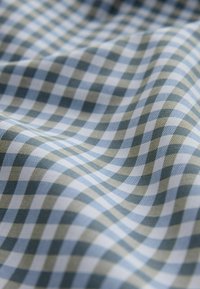 Tissu vichy bleu, blanc et vert olive avec un petit motif à carreaux, présenté avec des plis doux et une texture apparente.