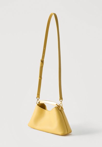 Κίτρινη δερμάτινη τσάντα ώμου με ρυθμιζόμενο λουρί και λείο καμπύλο χερούλι σε απλό λευκό φόντο.