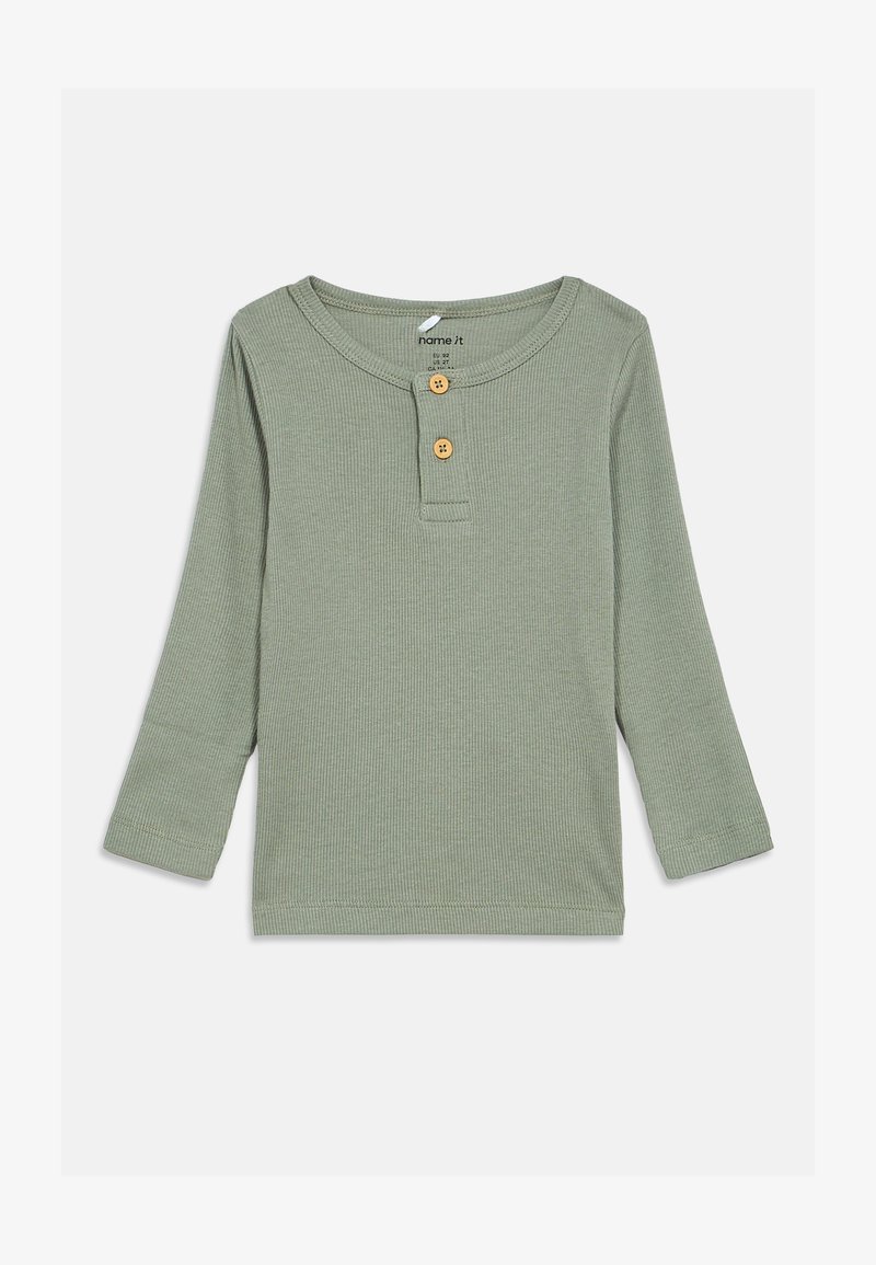 Garie rasos piedurkņu henley krekls mīkstā, ribotā audumā. Marķēts zaļā krāsā ar apaļu kakla izgriezumu, divām koka pogām un izšūtām apmalēm.