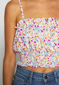 Blommig crop top med vit botten och färgglada mönster, volangkant vid halsringningen och resår i midjan. Matchas med denimshorts.