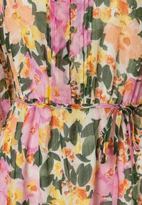 Bloemendress met een roze, gele en groene patroon, een knoopsluiting aan de voorkant, een stoffen riem en een lichtgewicht, gestructureerd materiaal.
