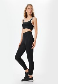 Svart atletisk outfit bestående av en kortärmad tanktop och högmidjade leggings, båda med en mjuk textur och kontrasterande vita kantdetaljer.