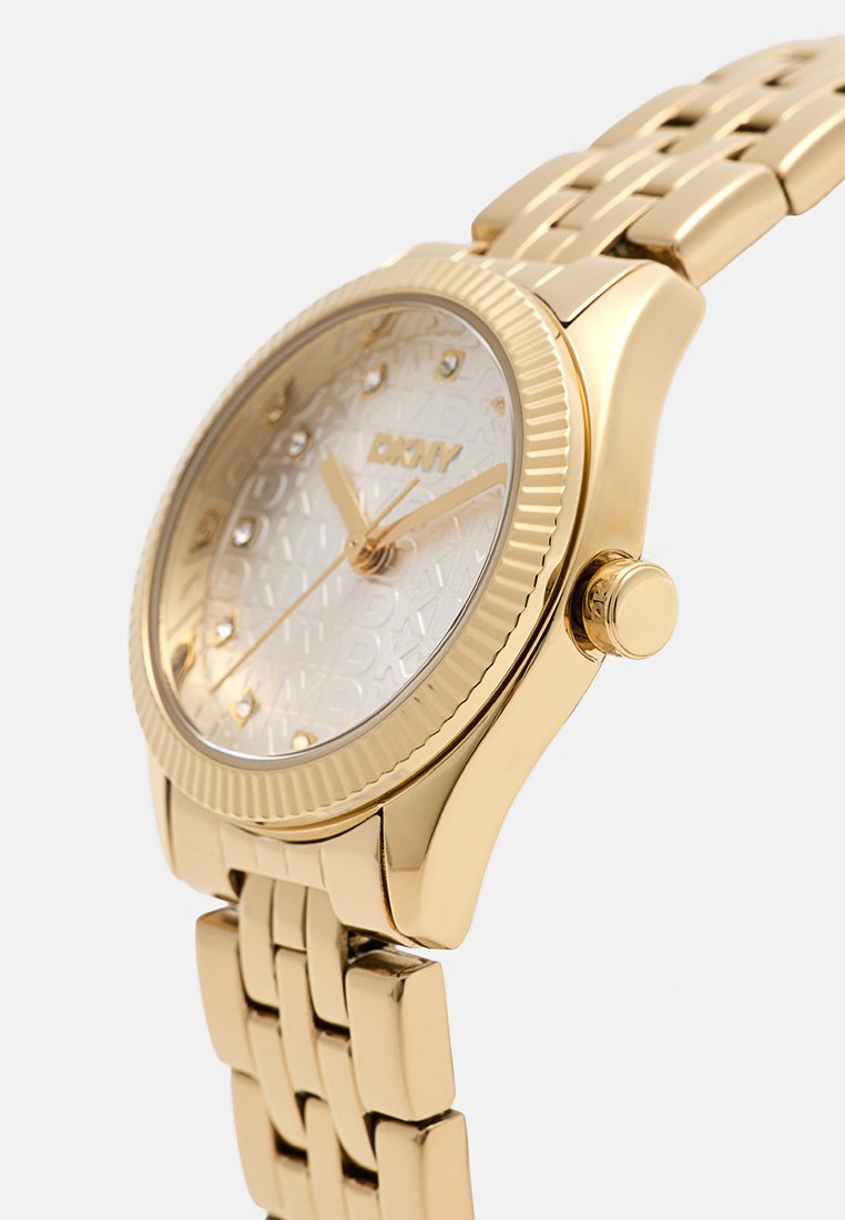 Reloj de metal en tono dorado con esfera de un gold suave texturizado, acentos de piedra y una esfera con patrón. Presenta un bisel estriado y un diseño de pulsera vinculada.