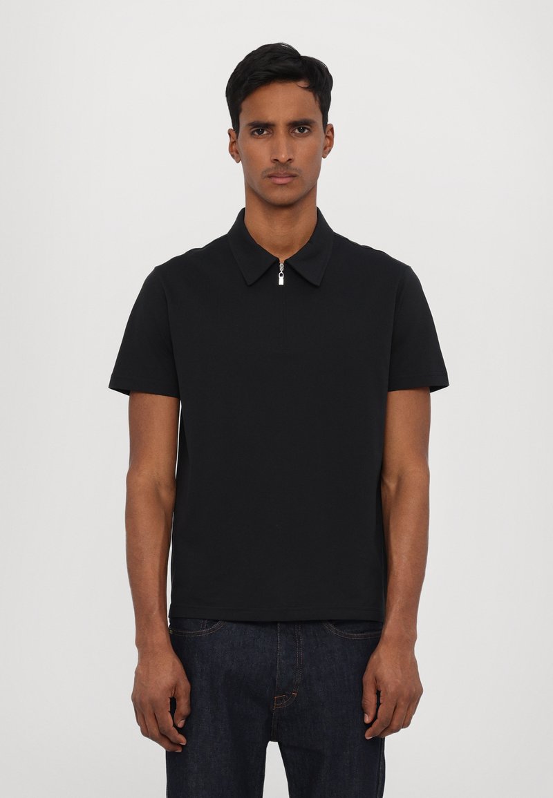 Polo preto de mangas curtas com colarinho plano e detalhe em zíper prateado no pescoço, confeccionado em tecido liso e sólido.