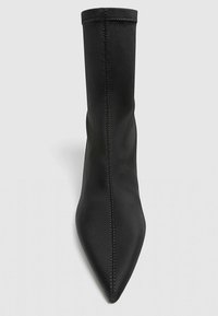 Bottines noires en tissu lisse avec un bout pointu et un design sans coutures, présentant des coutures visibles le long des bords.