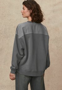 Grijze sweatshirt met een contrasterende, lichtere schouderpaneel, losse pasvorm, ribgebreide manchetten en ronde halslijn, gecombineerd met donkere denim jeans.