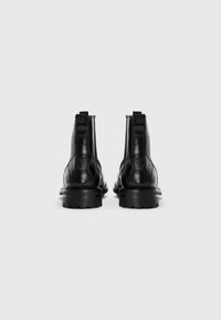 Botas de tobillo de cuero negro con textura suave, puntera redondeada y gruesa suela de goma negra. Presentan un logo grabado en la parte posterior.