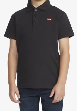 Child wearing a black short-sleeve polo shirt with a red Levi’s logo on the chest and dark blue jeans.