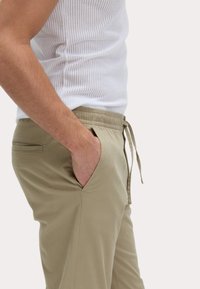 Lichtbeige herenbroek met een elastische tailleband en trekkoord, voorzien van zijzakken en een gladde, lichte stof.