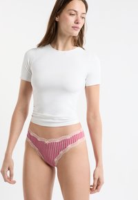 Biała dopasowana koszula z krótkimi rękawami, zestawiona z różowymi majtkami w paski z koronkowym wykończeniem i małą kokardką na pasku.