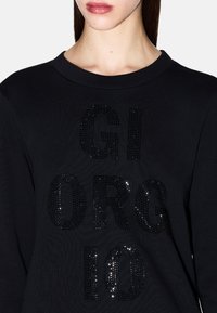 Sudadera negra con letras grandes de strass negro brillante que dicen "GIORGIO". La tela tiene un aspecto texturizado y un diseño de cuello redondo.