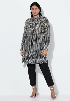Tunique rayée noir et blanc avec col, manches longues et coupe droite, associée à un pantalon noir et des sandales à talons blancs.