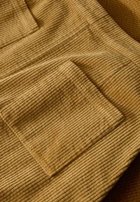 Sarkanas dzeltenas kordūrā audums ar vertikālām ribām, ar kabatpalikni. Tekstūra šķiet mīksta un izteikti svītraina.