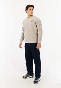 Lichtgrijze sweatshirt met een ronde hals en een klein logopatch, gecombineerd met donkerblauwe spijkerbroeken en zwarte sneakers met witte accenten.
