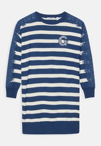 Svetrové šaty s námořnickými pruhy v kr�émové barvě, zdobené krajkovými akcenty na rukávech a kamínkovým logem "G" na hrudi. Měkký pletený materiál.