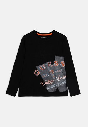 Schwarzes Langarm-Shirt mit Rundhalsausschnitt, vorne mit orange-weißem Text und Grafik "GUESS Vintage Denim Genuine Goods".