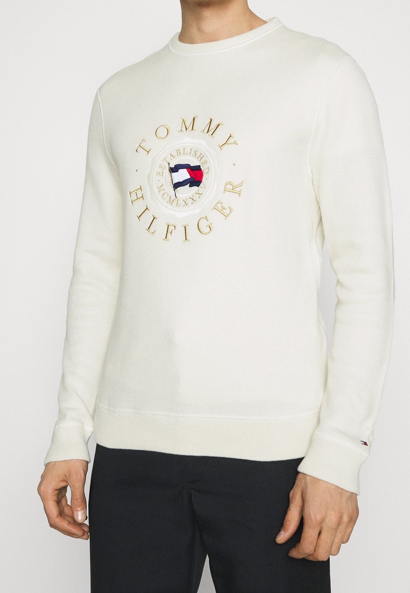 Weißes Baumwoll-Sweatshirt mit Rundhalsausschnitt, auf der Brust mit einem großen gestickten runden Logo in Gold und mehrfarbigen Akzenten versehen.
