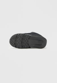 Suela exterior de zapato deportivo negro con goma texturizada para agarre, presenta una banda de rodadura con patrón y un detalle sutil de logotipo. Forma rectangular.