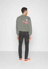 Gray sweatshirt with text and pink design on the back, paired with black jeans and orange-striped sneakers. Smooth texture, casual fit.