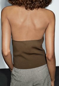 Top senza spalline marrone a coste abbinato a pantaloni a righe grigio chiaro, che mostra una schiena liscia e un design minimalista; senza hardware visibile.