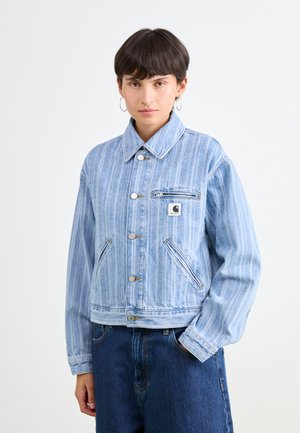 Lys blå denimjakke med vertikale striper, spiss krage, trykknapper og en brystlomme. Har løs passform og elastiske mansjetter.