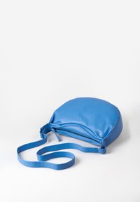 Blaue, weich strukturierte, synthetische Umhängetasche mit flachem Design, langem Gurt und Reißverschluss. Schlichte, geschwungene Form ohne zusätzliche Akzente.