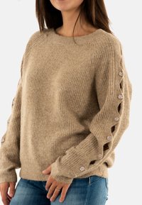 Maglione lavorato a maglia beige con texture a coste, caratterizzato da bottoni decorativi lungo le maniche e una vestibilità rilassata.