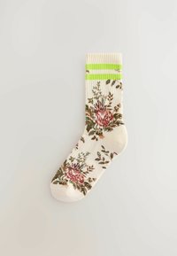 Knæhøje sokker lavet af blødt stof med et blomstermønster i pink og grønt på en cremefarvet baggrund, med grønne og hvide stribede detaljer øverst.