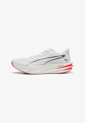 Hvid løbesko med sort Puma-logo, tyk skulpturel sål og røde accenter på hæl og ydersål.
