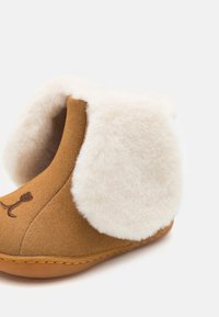Brune tøffel med en semsket overflate, hvit faux pelsovering, rund form, og et brodert hundefjesdesign på fronten.