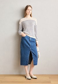Chunky gebreide trui in crèmekleur met lichtblauwe strepen, gecombineerd met een mid-length, donkerdenim rok met een split aan de voorkant. Klassieke platte schoenen.