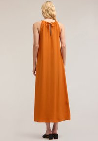 Vestido largo sin mangas de tela naranja con un escote en forma de ojo de cerradura y cintas ajustables en el cuello. Textura suave y diseño fluido.