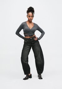 Γκρι μακρυμάνικη εμπρός τοπ με κόμπο, σε συνδυασμό με ψηλόμεσα, φαρδιά μαύρα τζιν, συνοδευόμενα από λαμπερά μαύρα παπούτσια με φαρδιά τακούνια.