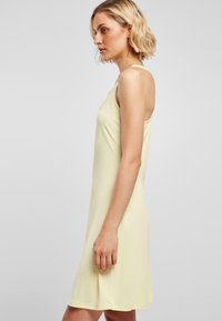 Vestido sin mangas de color amarillo claro con un corte holgado, hecho de una tela suave, con escote redondeado y un dobladillo acampanado.