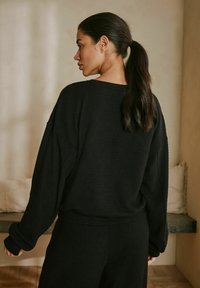 Schwarzer, strukturierter, übergroßer Pullover mit langen Ärmeln, weitem Ausschnitt und lockerer Passform, kombiniert mit passenden schwarzen Unterteilen. Dezentes Rippmuster.