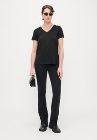 Sort V-hals T-shirt med korte ærmer, struktureret stof med subtile flerfarvede prikker, parret med sorte flared bukser og ankelstøvler.