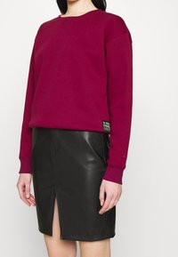 Sudadera burdeos con puños y escote acanalados, combinada con una falda de cuero negro con una abertura frontal para un look moderno.